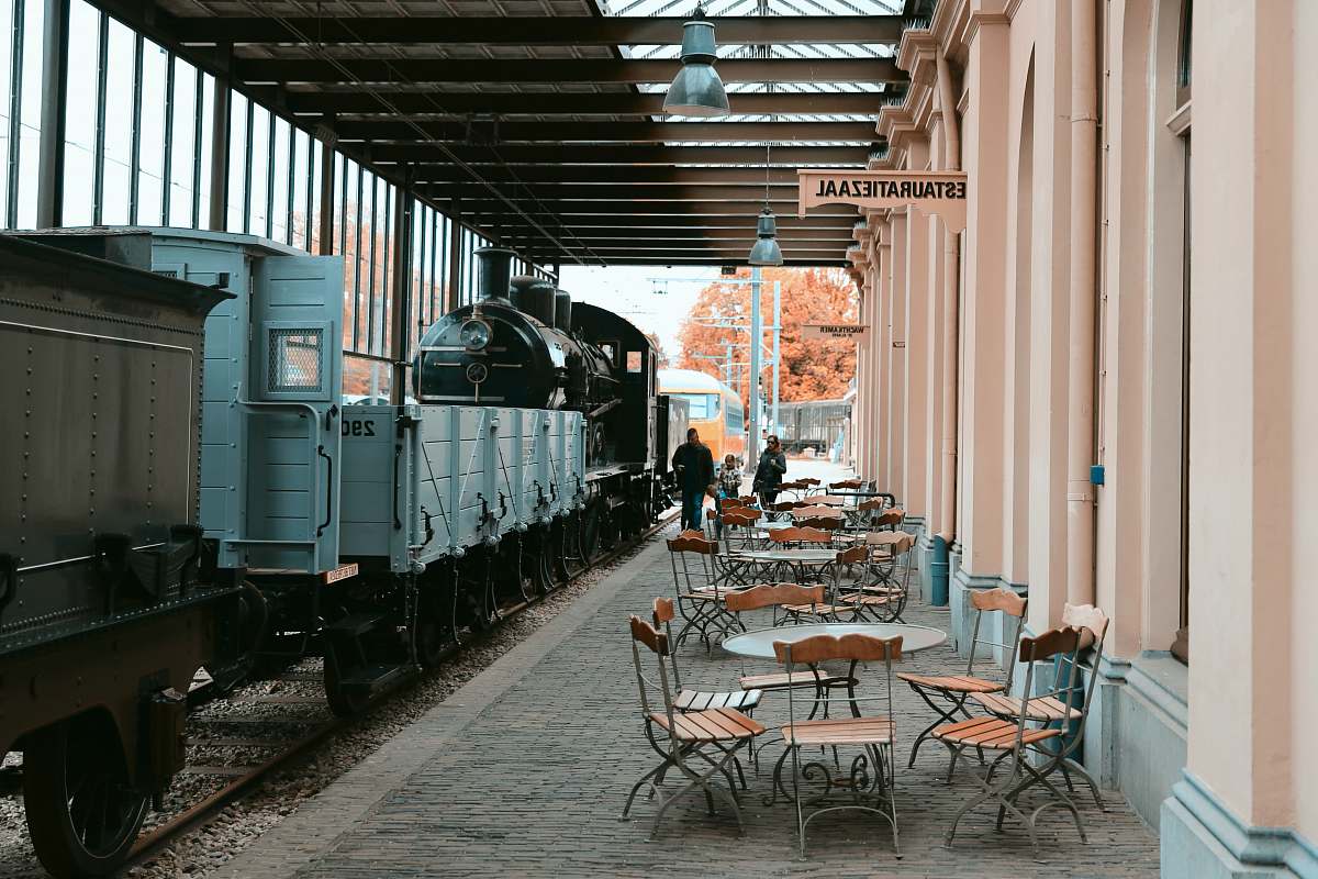 chair three people walking in alley with cafes and parked train furniture