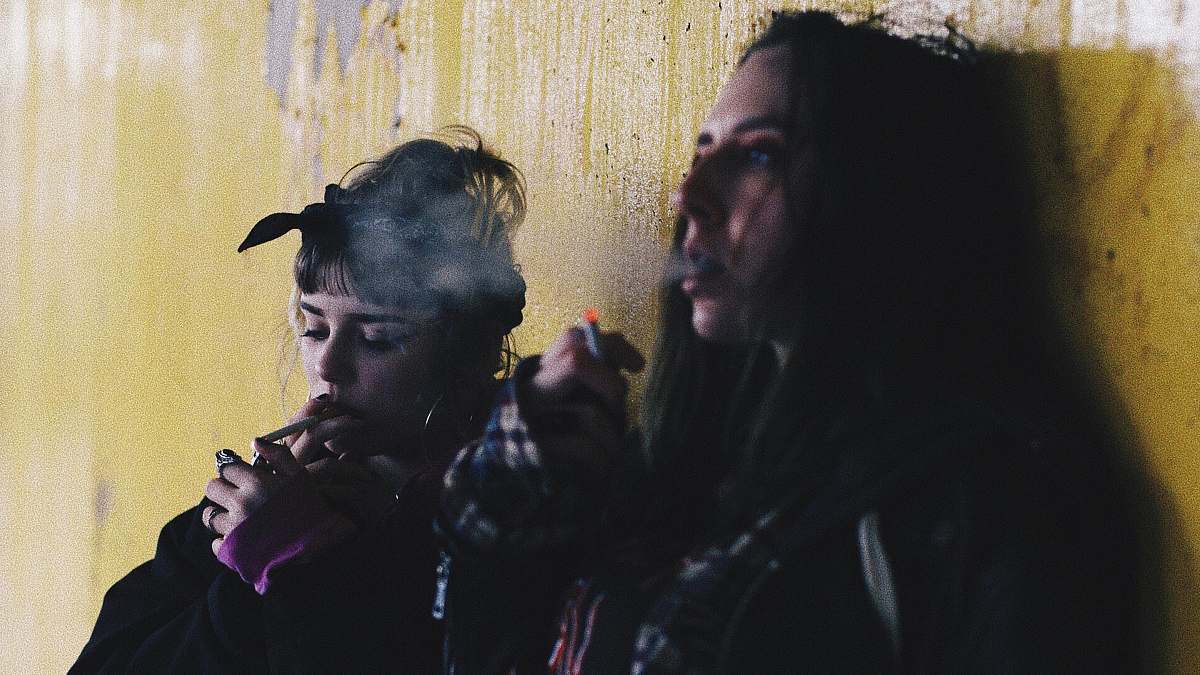 person two women smoking while leaning on yellow wall people