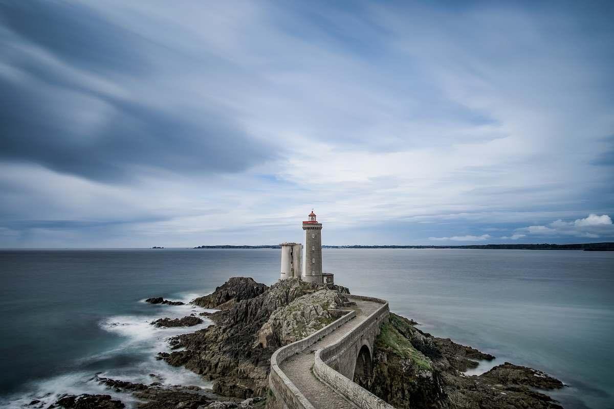 sea grey concrete lighthouse on cliff surrounded body of water during daytime water