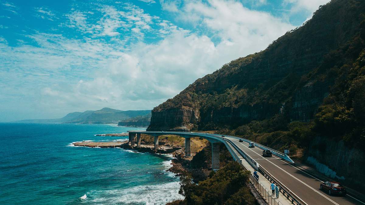road photography of black concrete road near body of water ocean