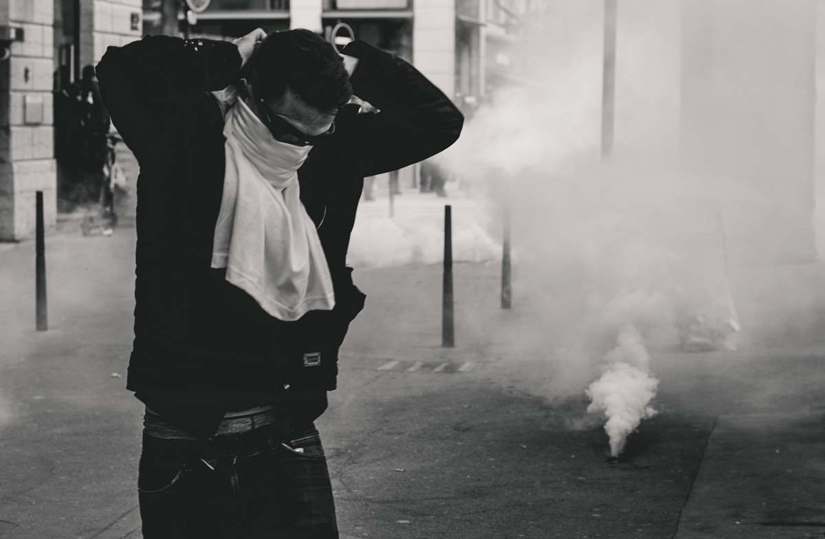 human man standing and covering his face using shirt smoke