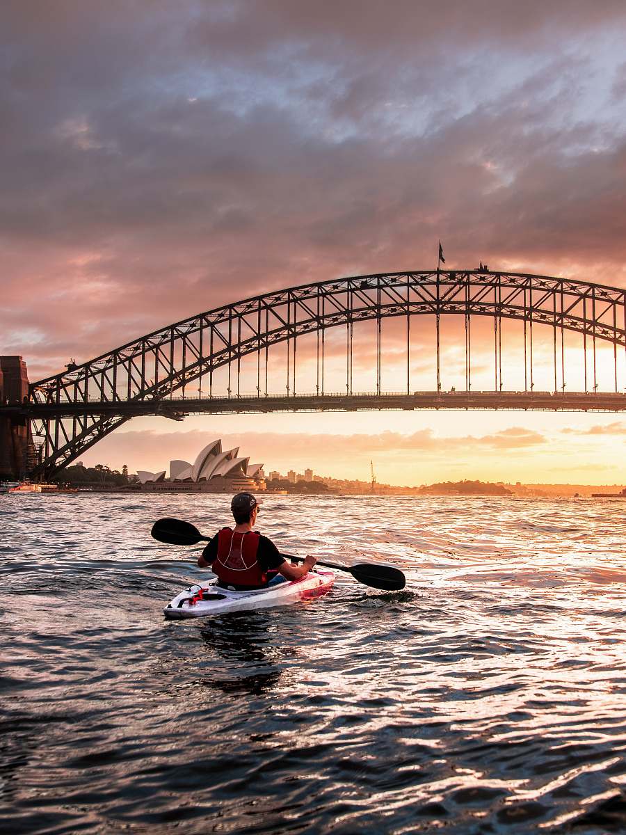 human person riding kayak towards metal bridge person