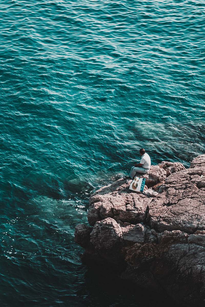 person man sitting on rock near body of water during daytime nature