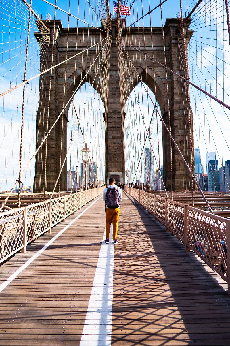 an in white shirt and yellow pants walking on bridge during daytome