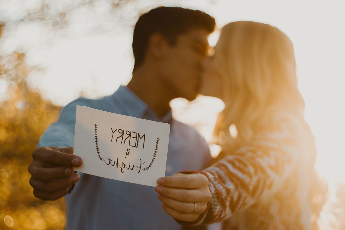 couple kissing while holding merry and bright signage