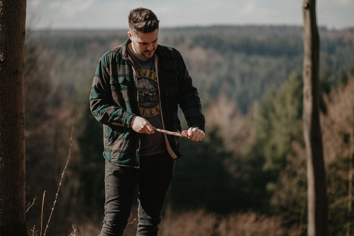 man in green and gray jacket holding brown stick near green leafed trees during daytime shallow focus photography