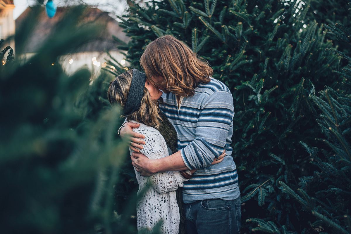 man kissing woman near pine tree