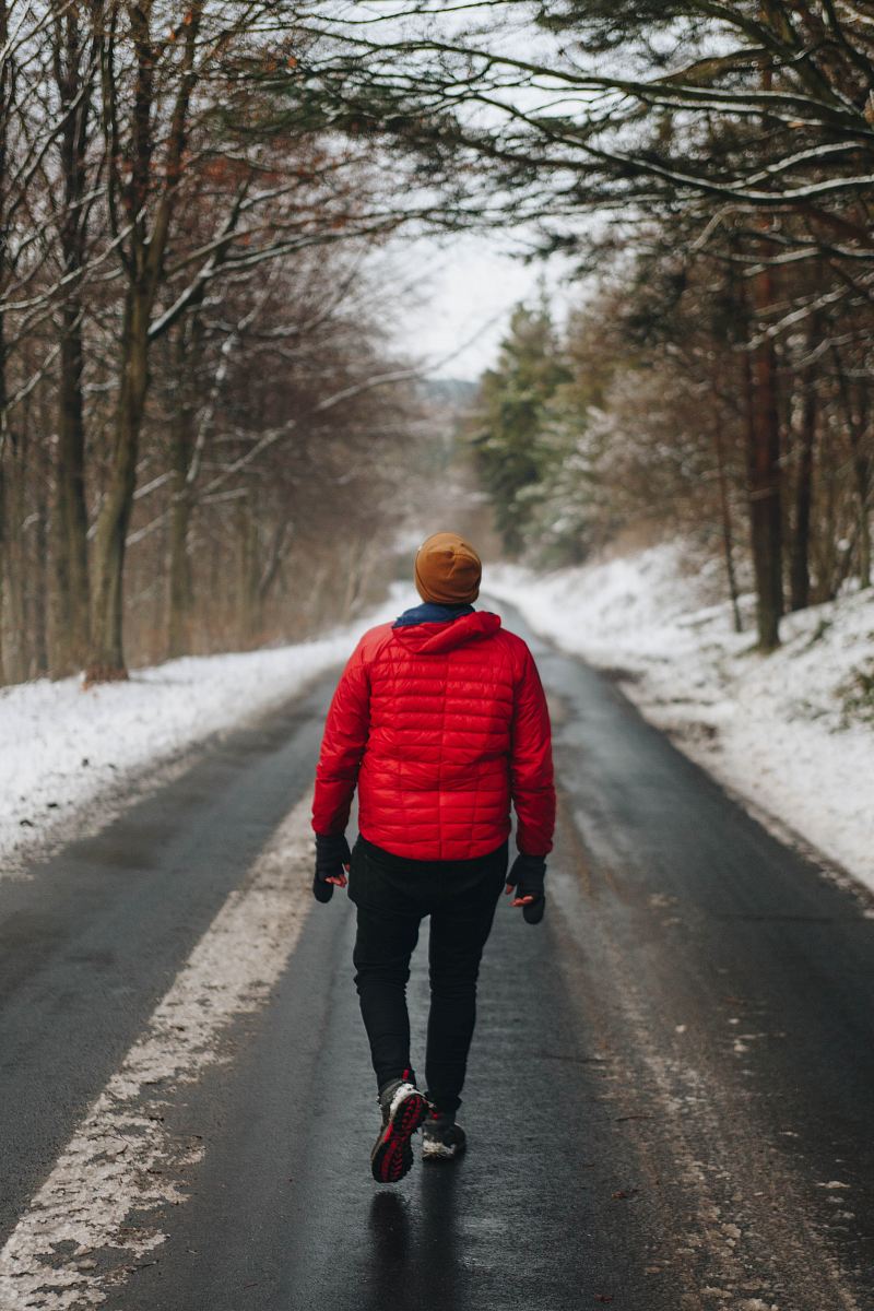 man walking on asphalt road at middle of leafless tree