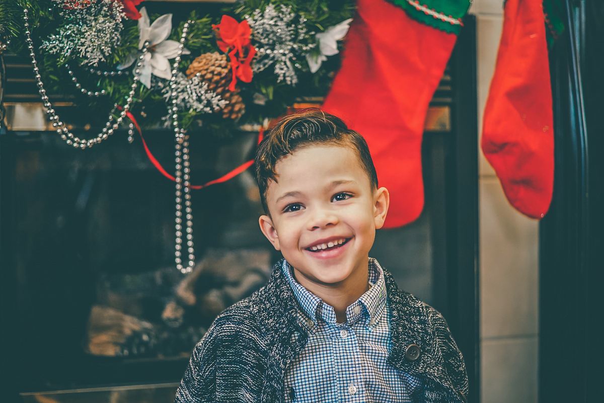 smiling boy in gray inner shirt and gray cardigan standing by fireplace with decors