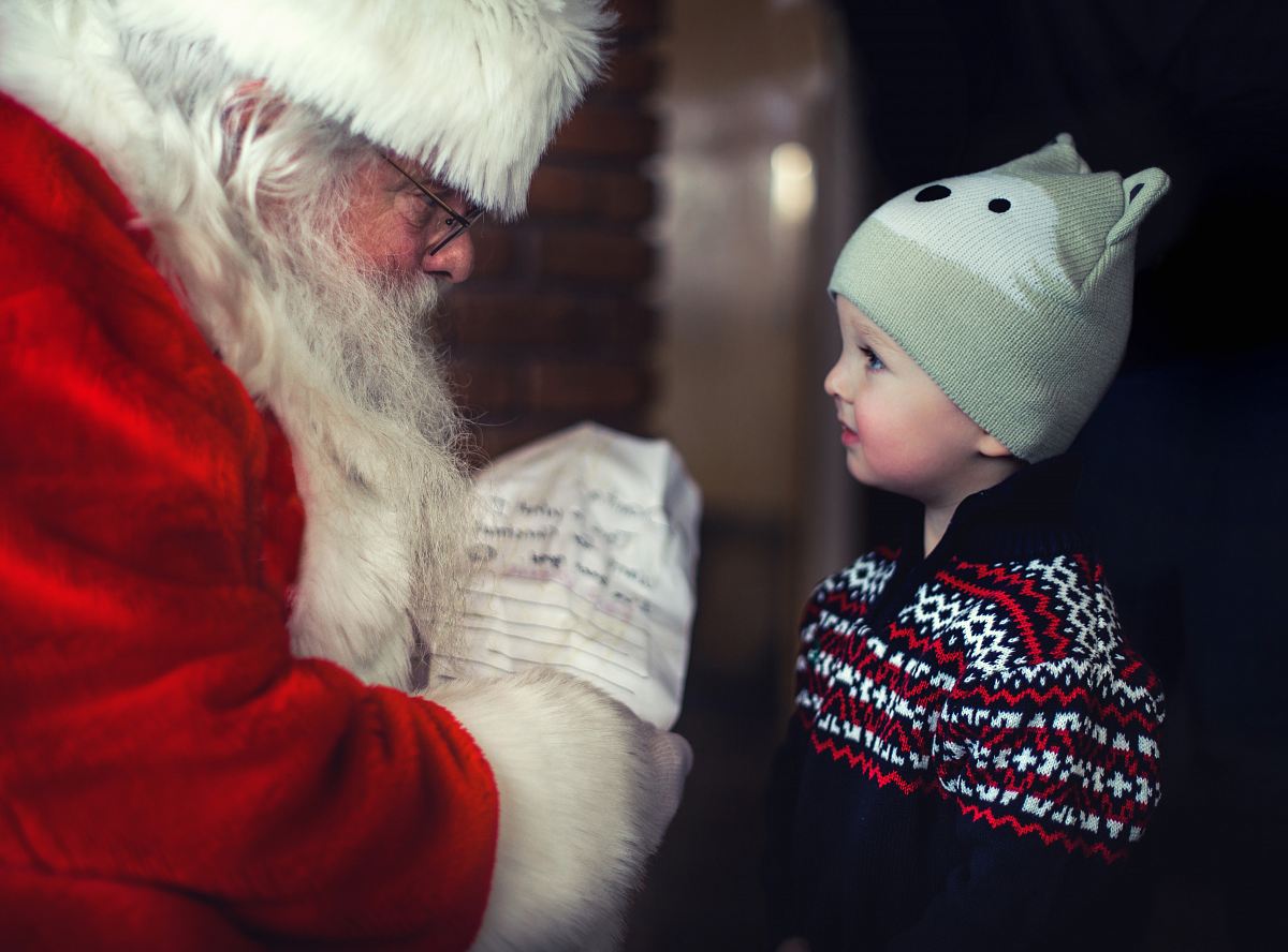 toddler in black sweater standing in front of Santa Claus