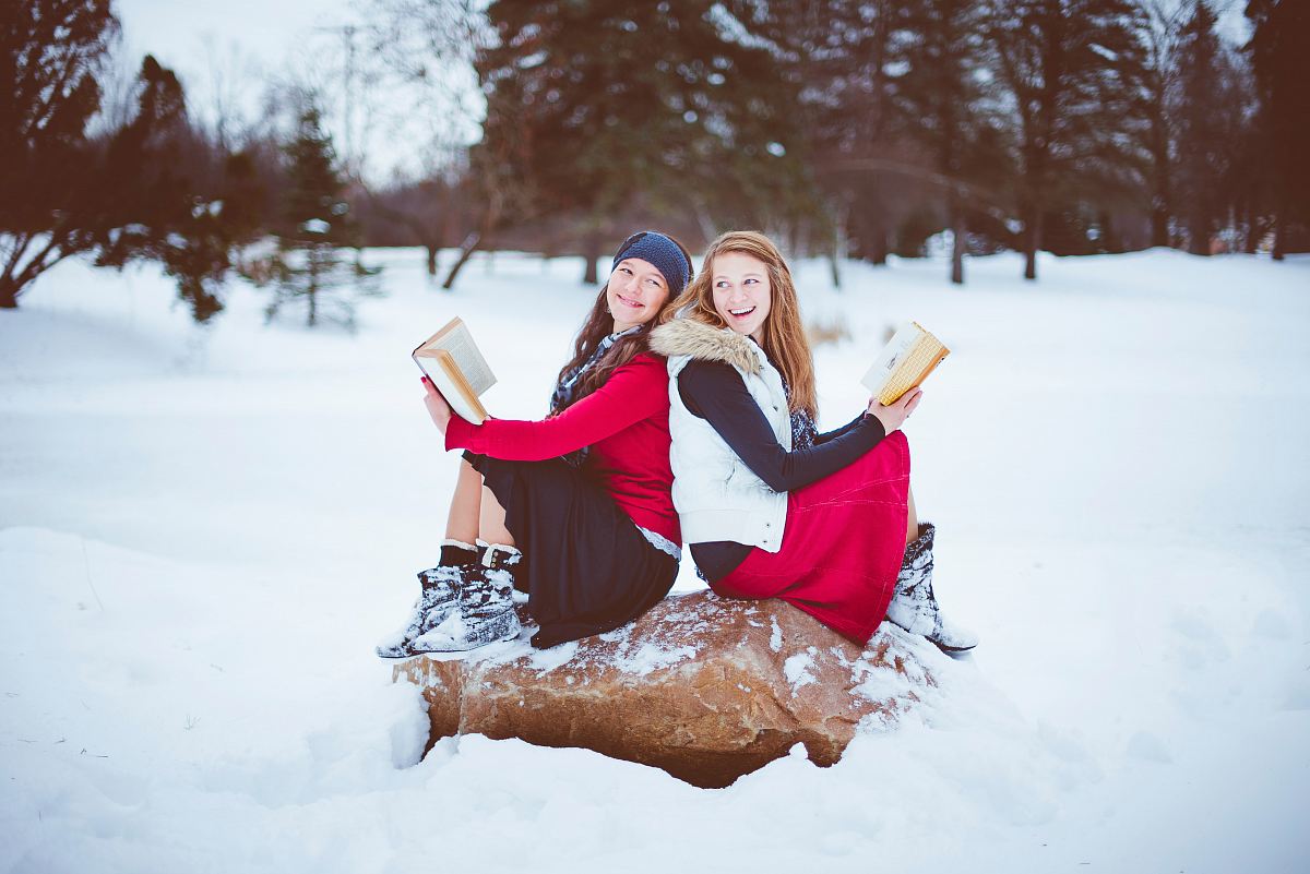 two women sitting on rock while holding books