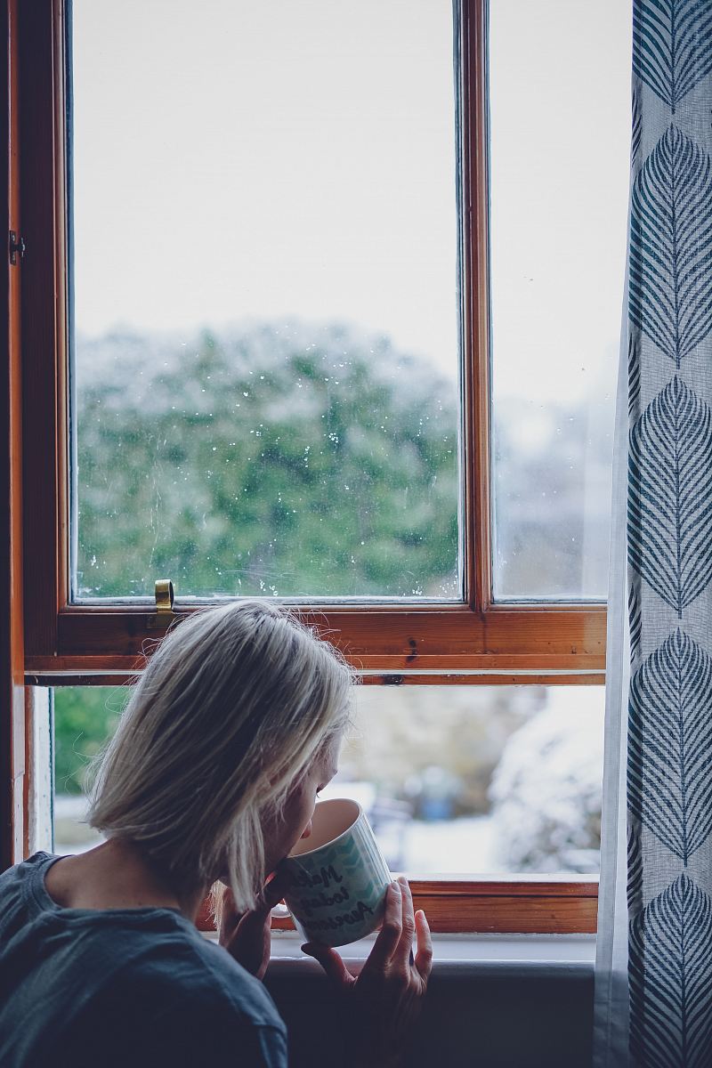 woman drinking in front of window at daytime