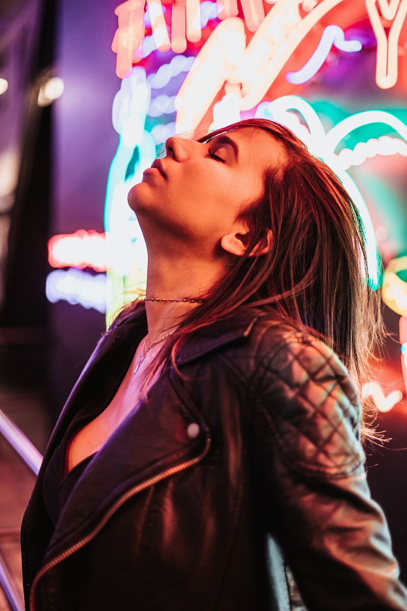 woman wearing black leather jacket standing near neon signage