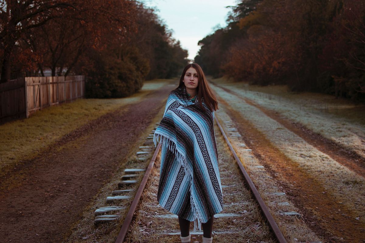 woman with blue and black striped scarf standing on brown train railway during daytime