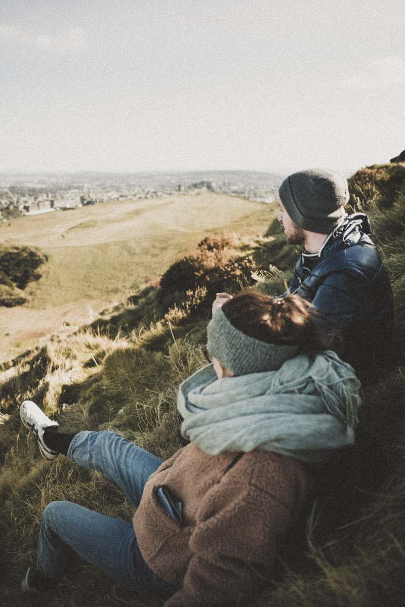  man and woman sitting on green grass while looking at city during daytime 