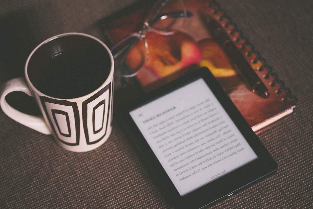 reading black E-book reader beside white and black mug coffee cup