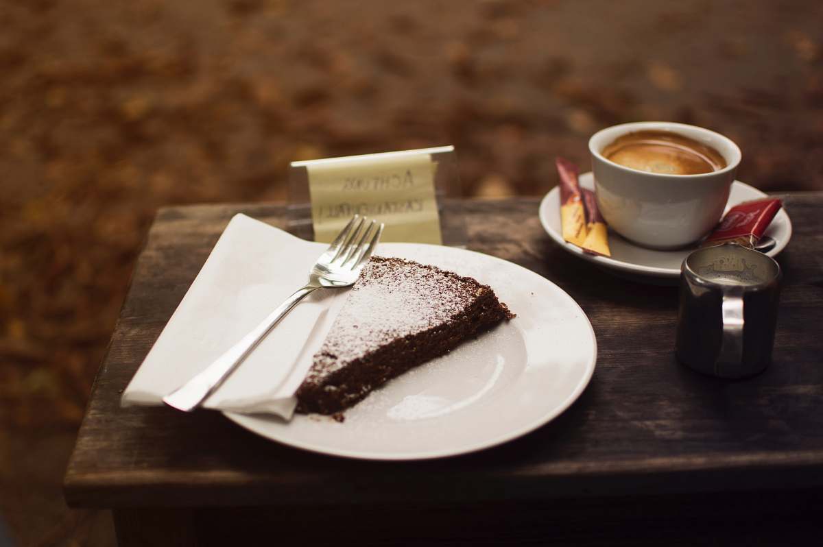 food plate of sliced cake with silver fork beside cup of coffe on brown wooden serving board dessert