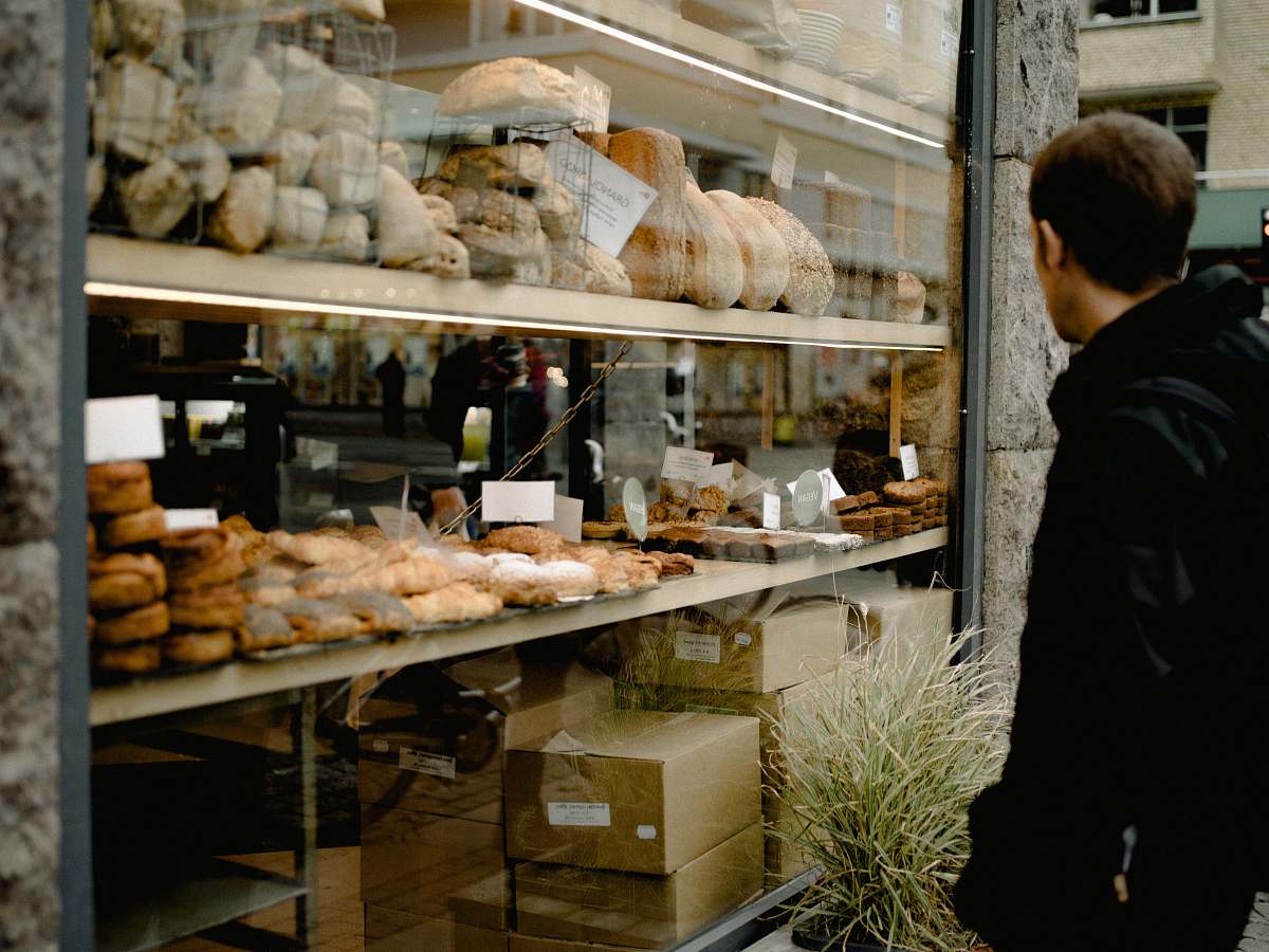 bakery man wearing black jacket standing near glass window bread