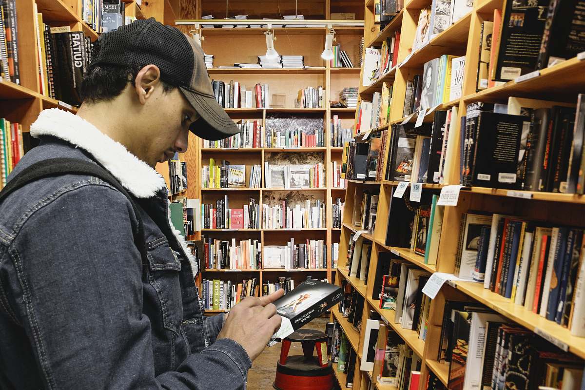 person man holding book beside bookshelf indoors