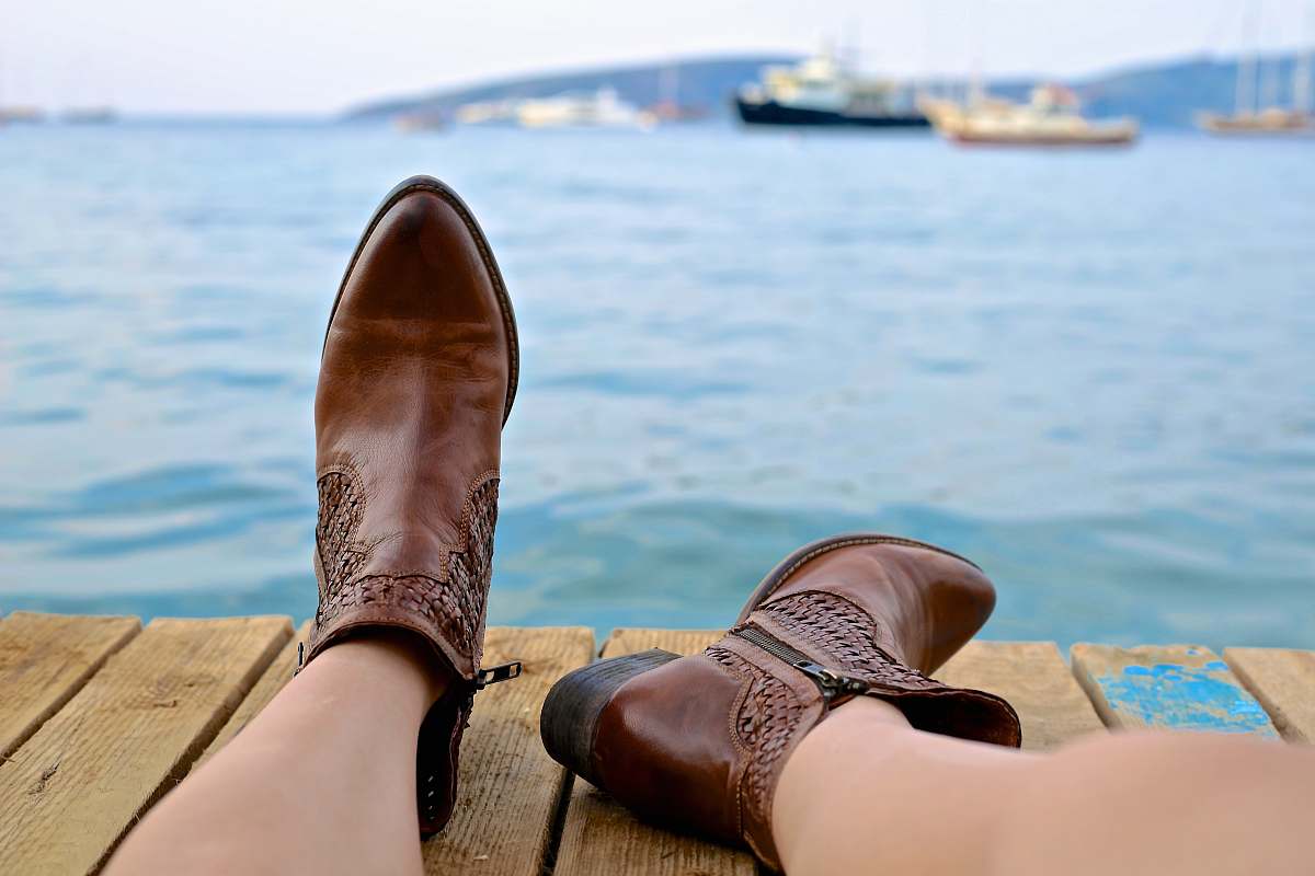 sea person wearing brown leather side-zip boots sits on brown wooden pier near body of water during daytime boot