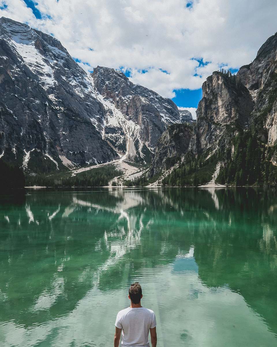 snow man standing in front of lake and cliff under white clouds and blue sky nature