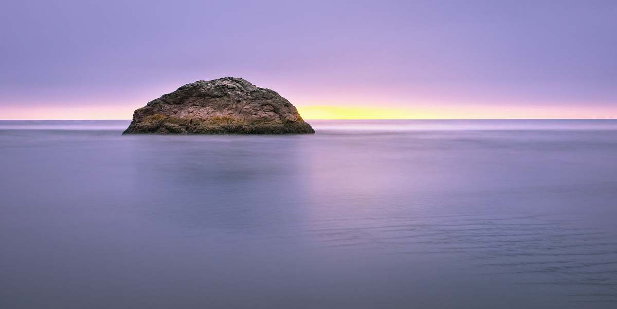 water landscape photography of brown rock formation in the middle of the ocean rock