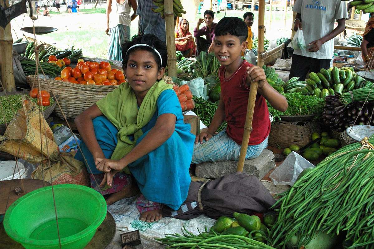 human girl and boy sitting between vegetables market