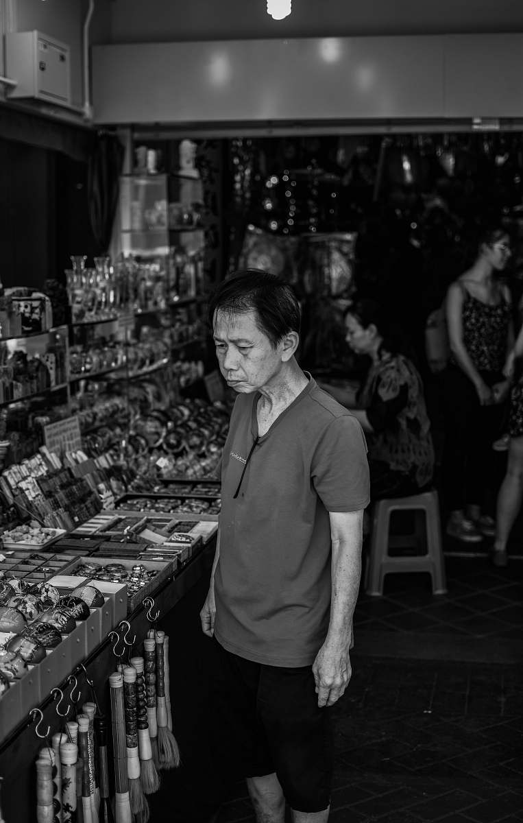 human grayscale photo of man stand in front of stall black-and-white