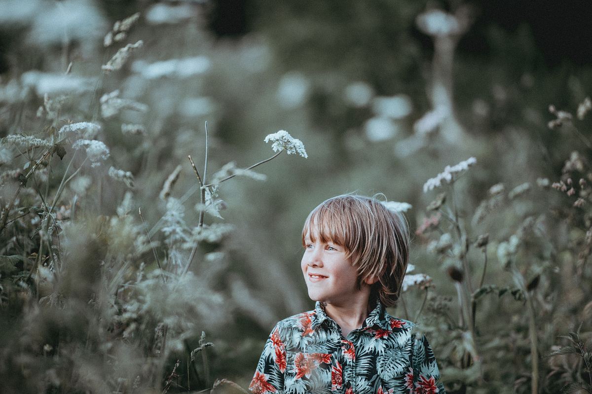 boy's red and green floral button-up collared top smiling facing grasses