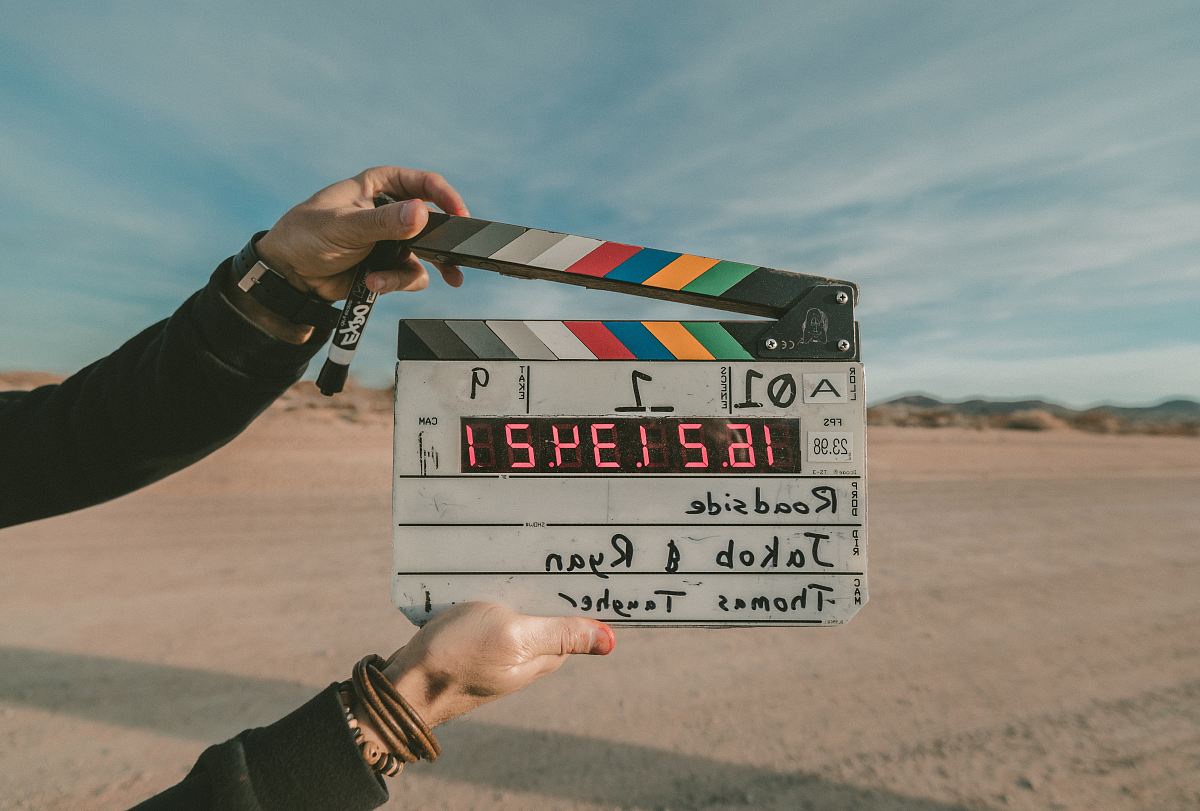 In this vibrant roadside setting, two friends, Jakob and Ryan, enthusiastically engage with a classic clapboard. The energy of their interaction brings a lively atmosphere to the scene, making it perfect for creative projects, film production, or social media content. This image captures the essence of spontaneity and collaboration, ideal for use in advertising campaigns, blogs about filmmaking, or content related to friendship and creativity.