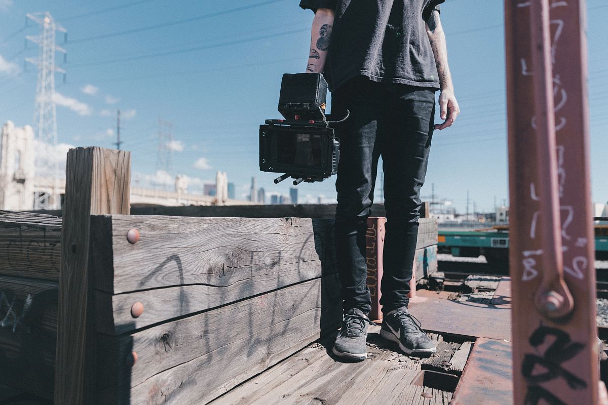 man holding black video camera while standing on plank