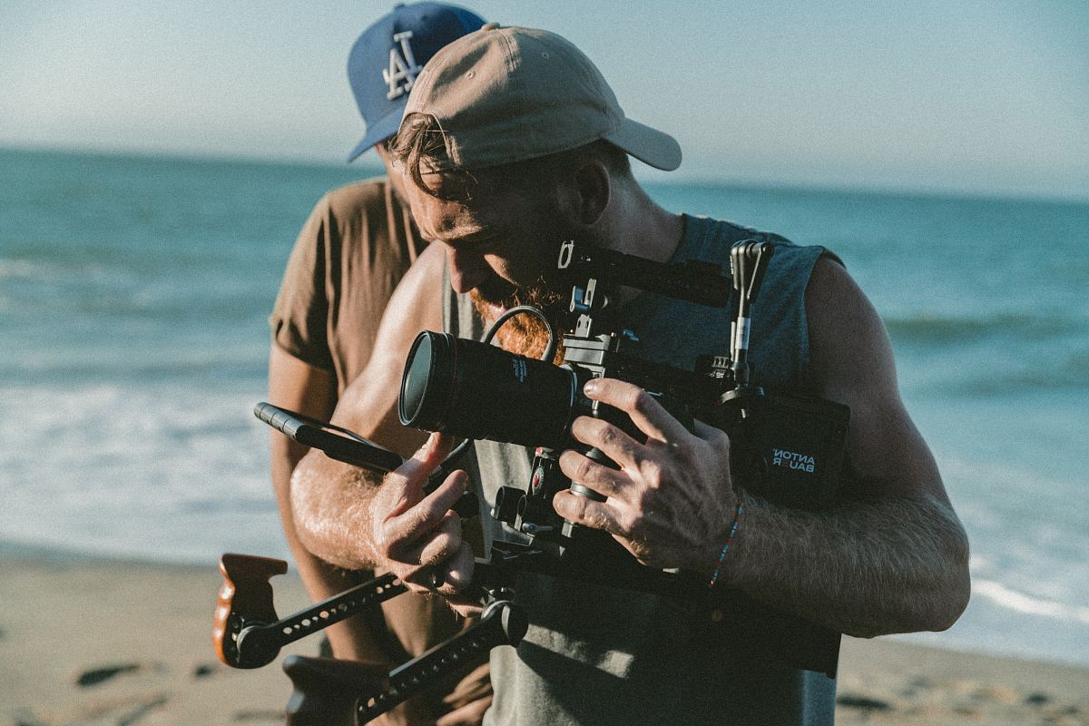 man holding video camera standing near body of water