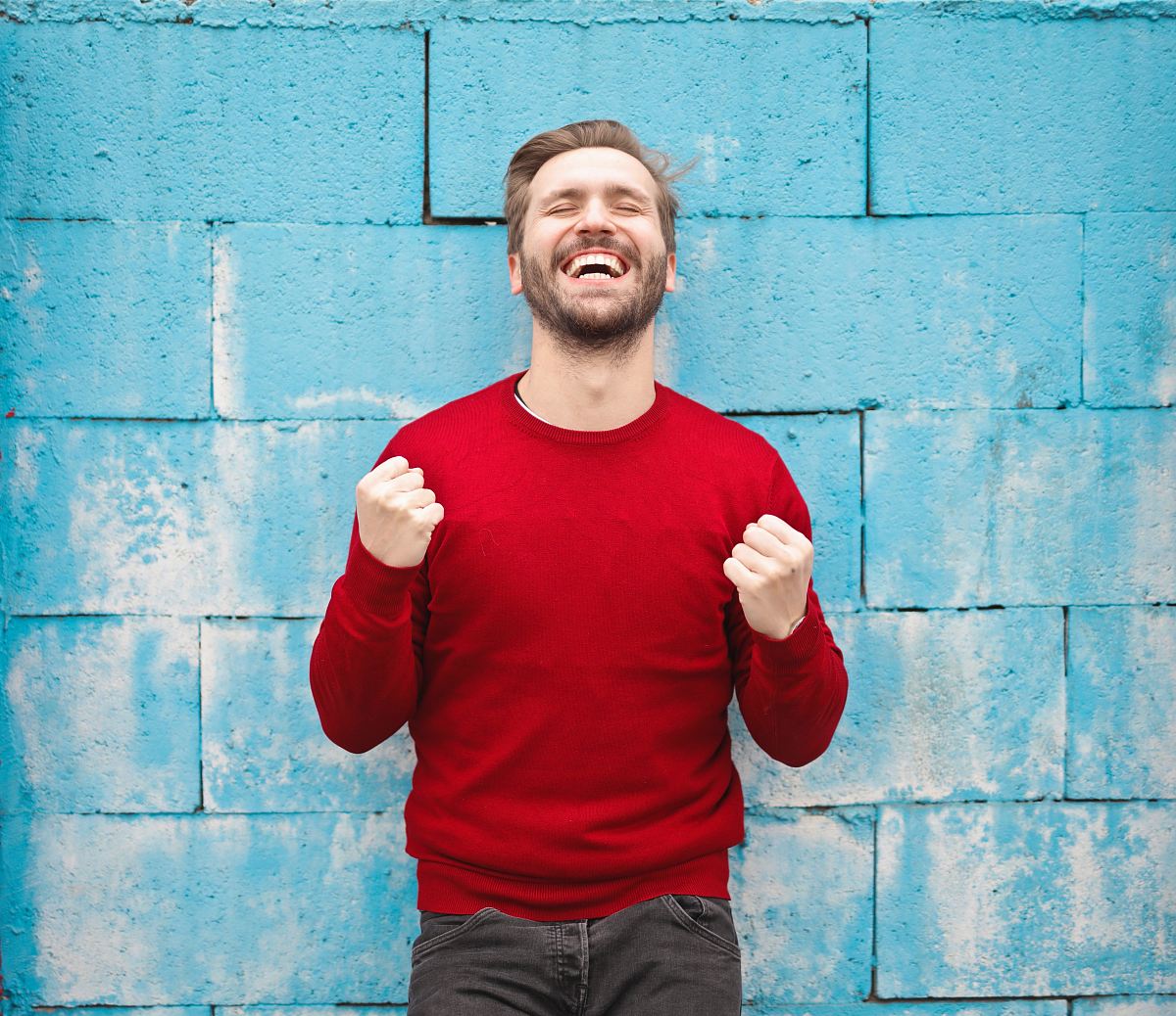 man wearing red long-sleeved shirt standing beside wall