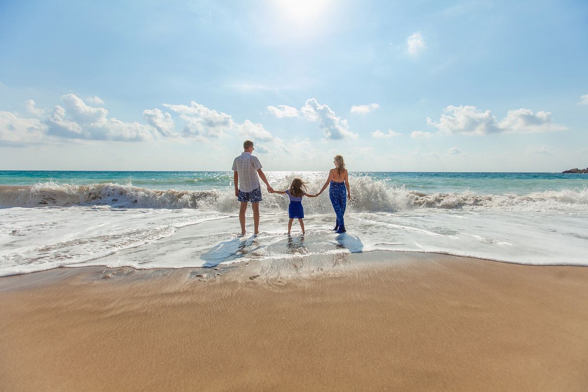 man, woman and child holding hands on seashore