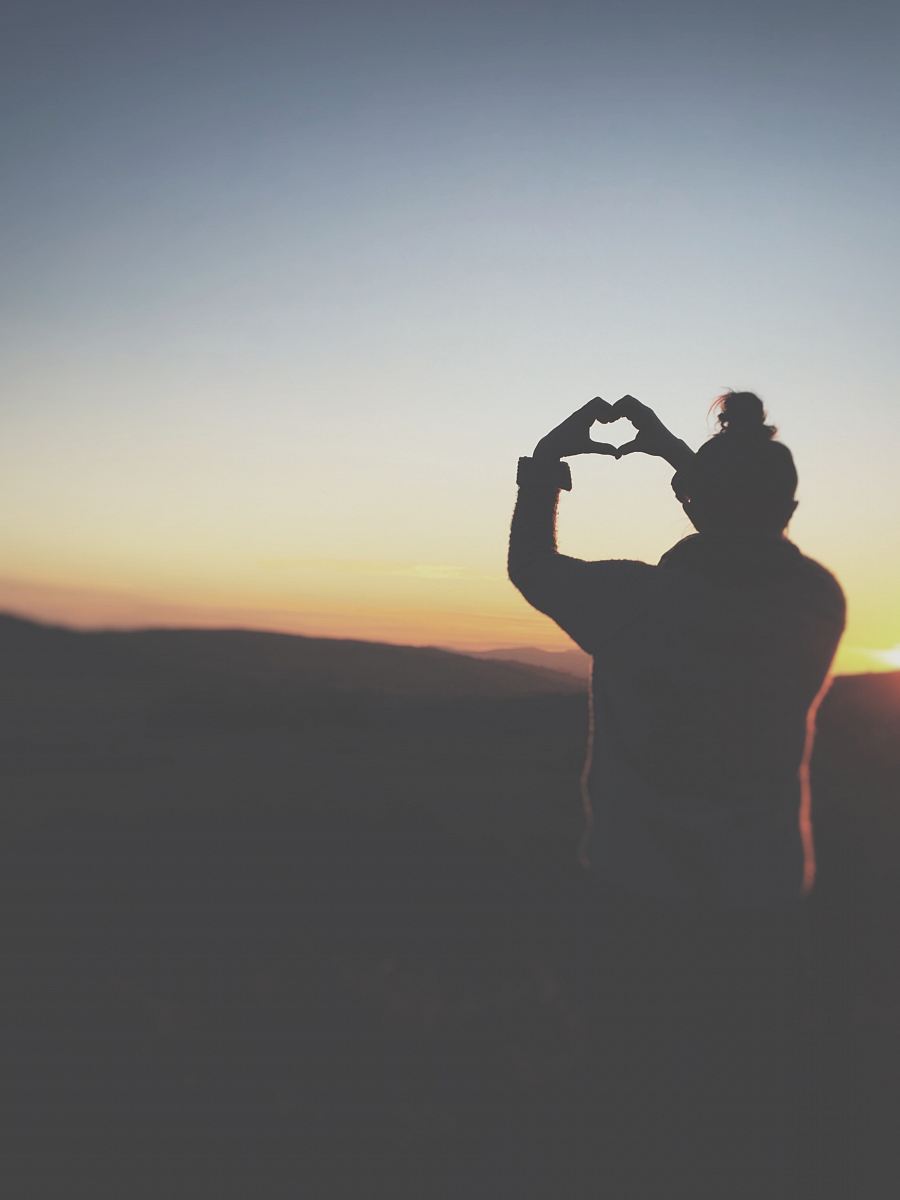 silhouette of a person making heart using her hands
