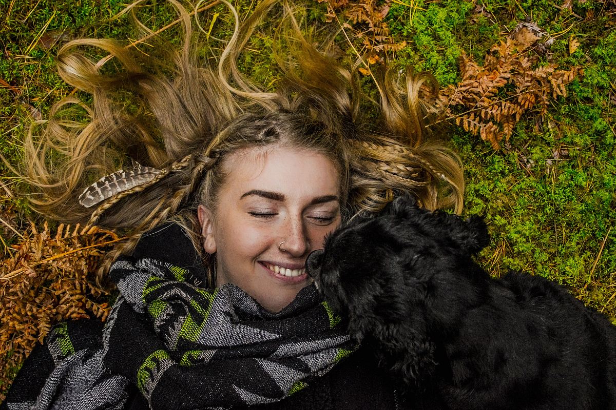 smiling woman lying on ground beside black dog at daytime