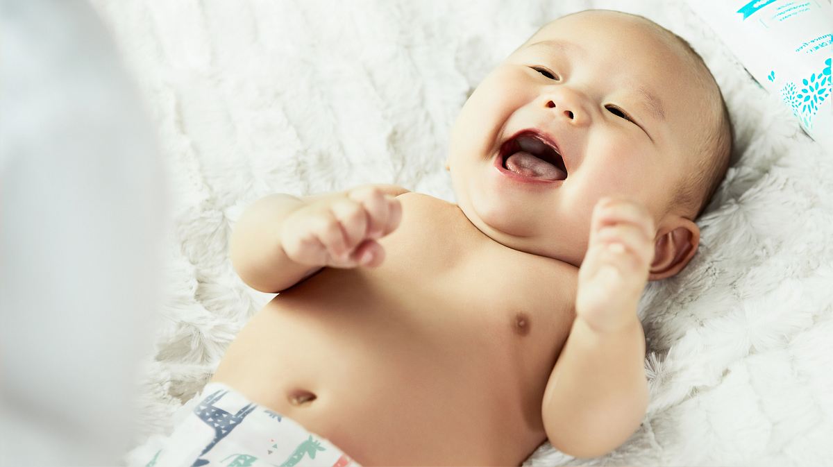 topless baby lying on bed smiling