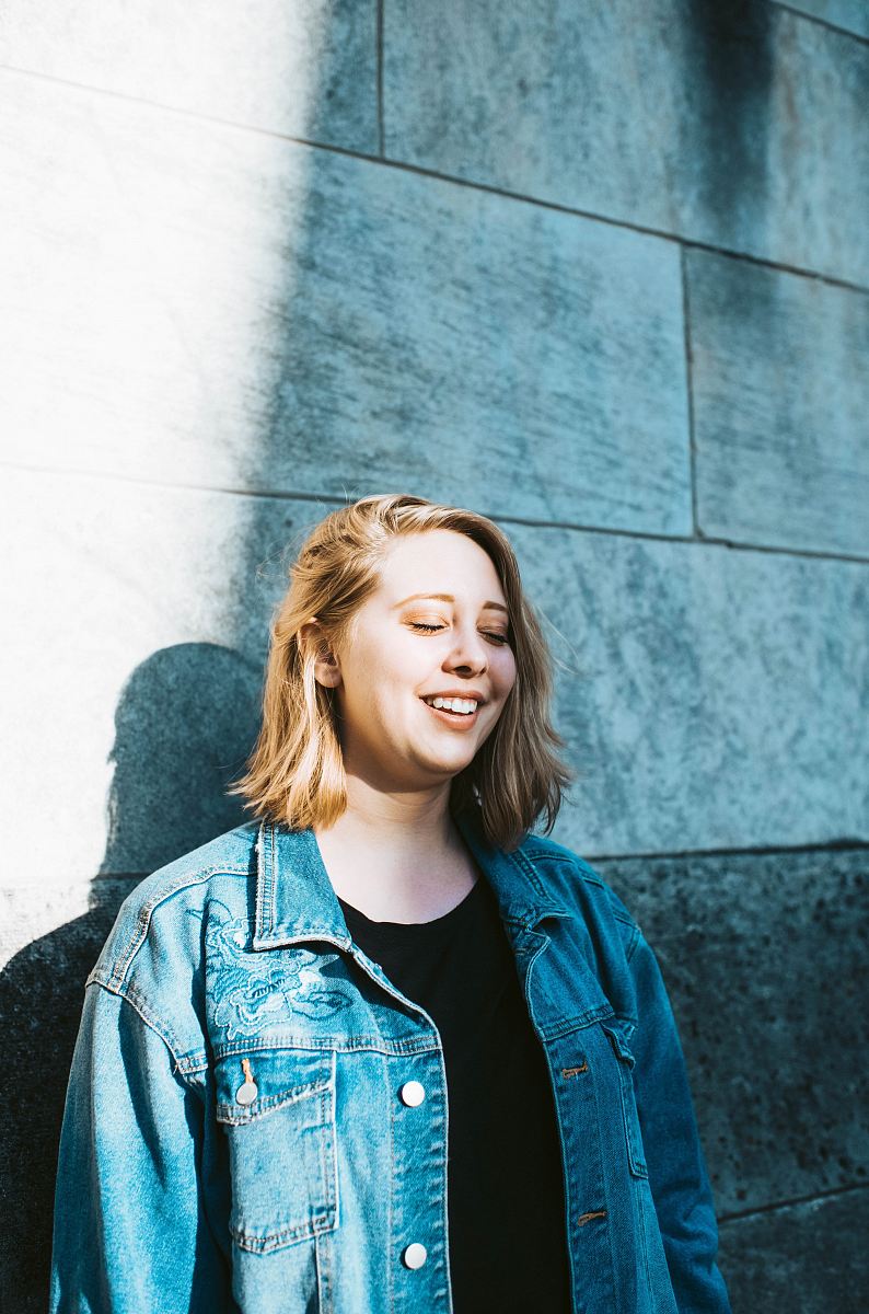 woman in blue denim jacket leaning on wall