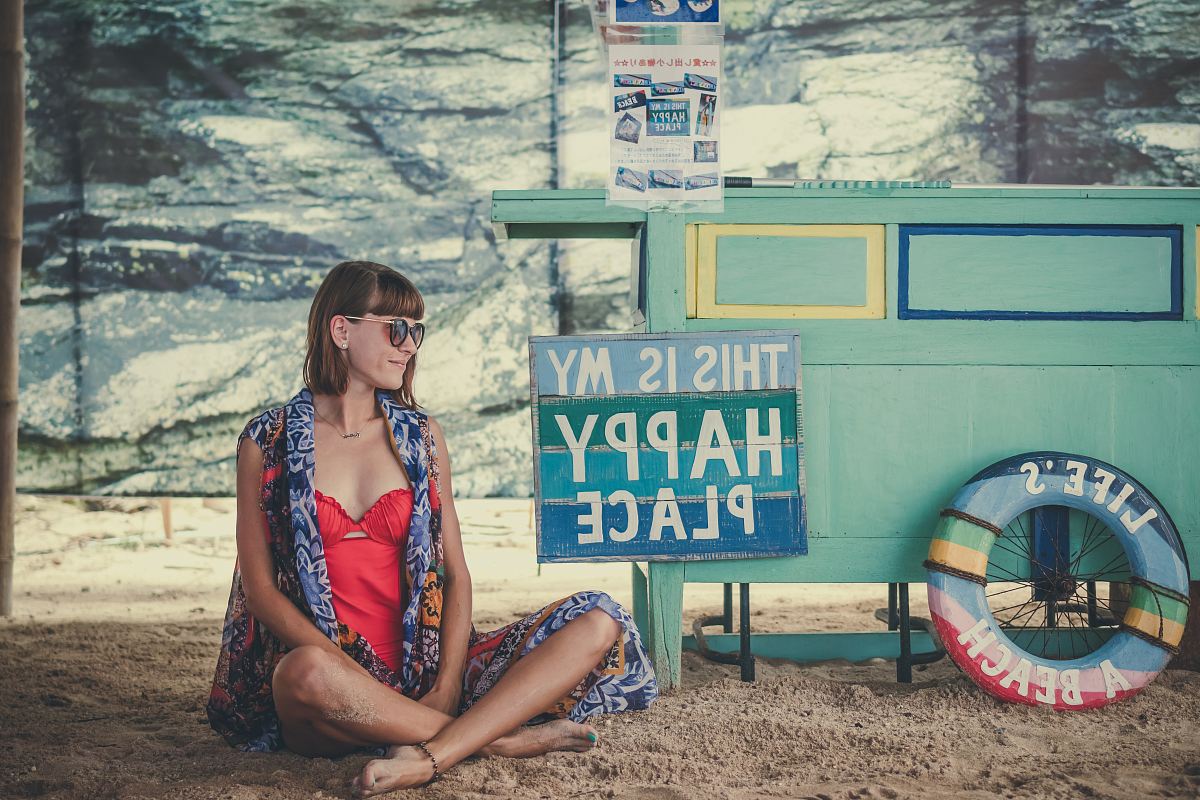 woman sitting on sand beside of This is My Happy Place signage