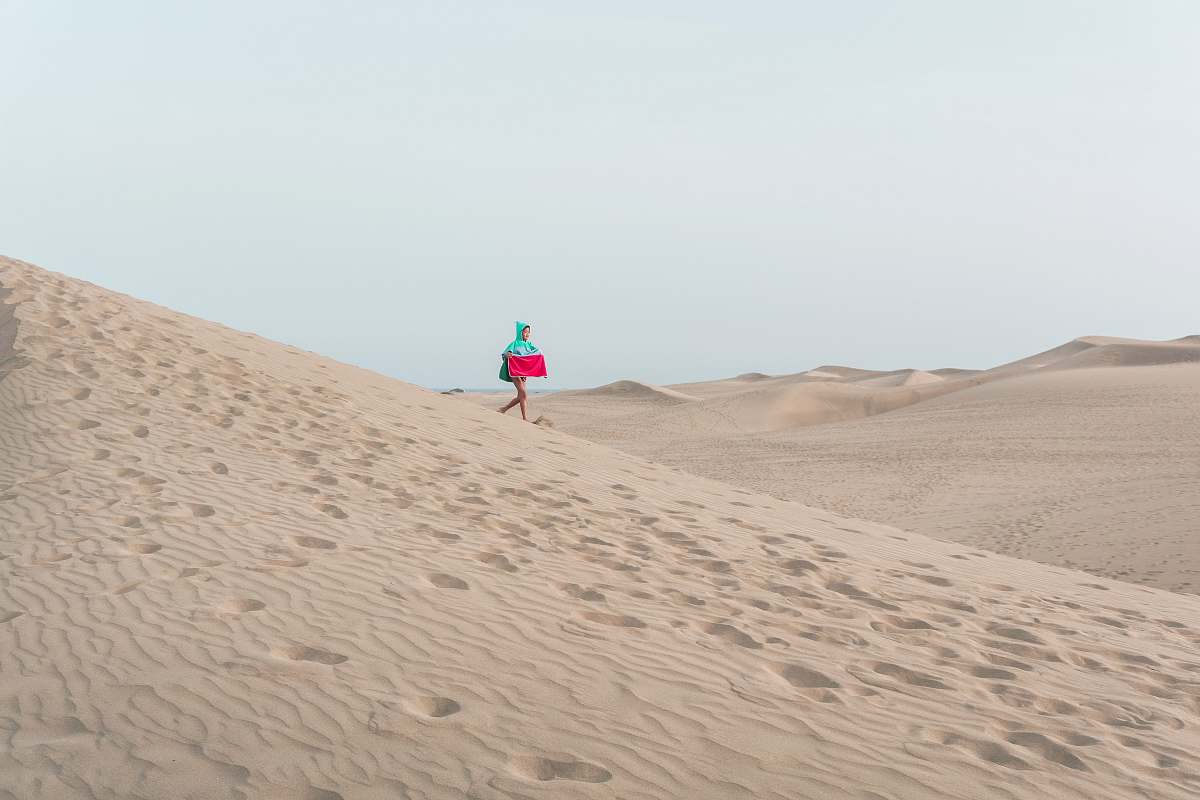 sand photo of person walking on desert holding red box soil
