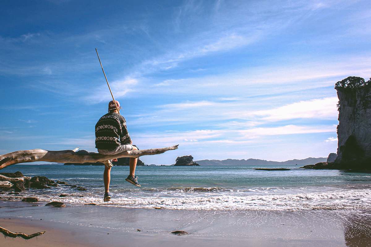 outdoors person sitting on driftwood near seashore during daytime water