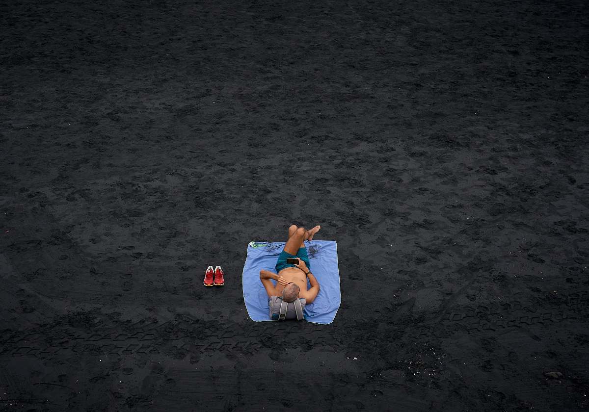 person shirtless man lying on blue picnic mat on the field sand