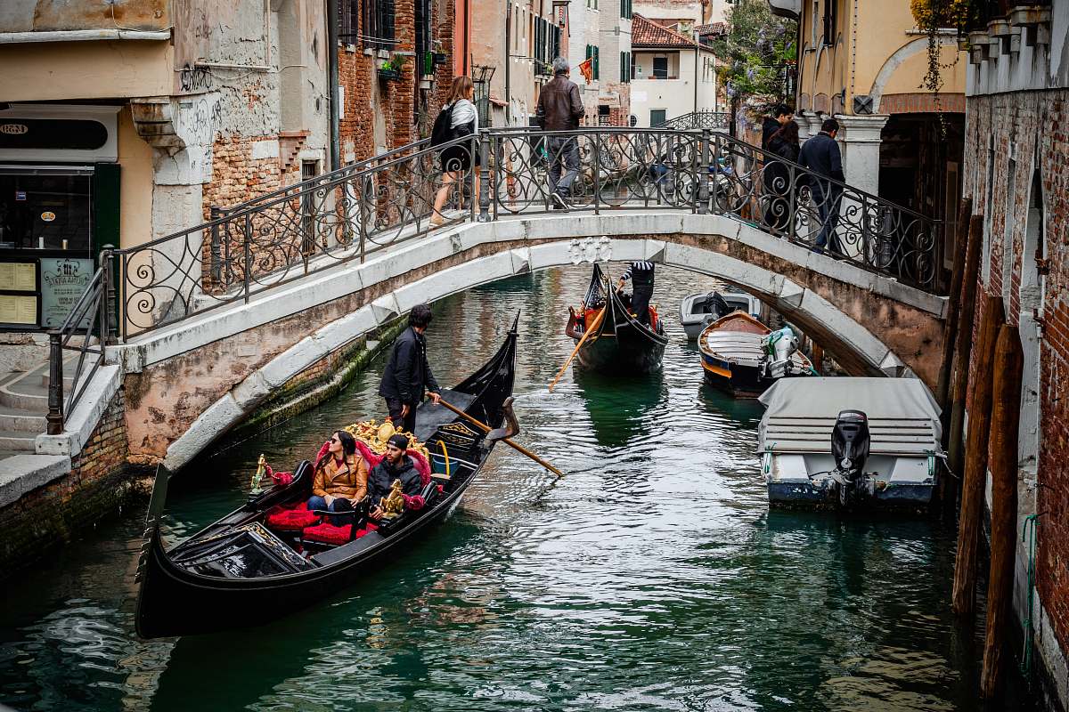 human people riding boat near bridge with people crossing during daytime gondola