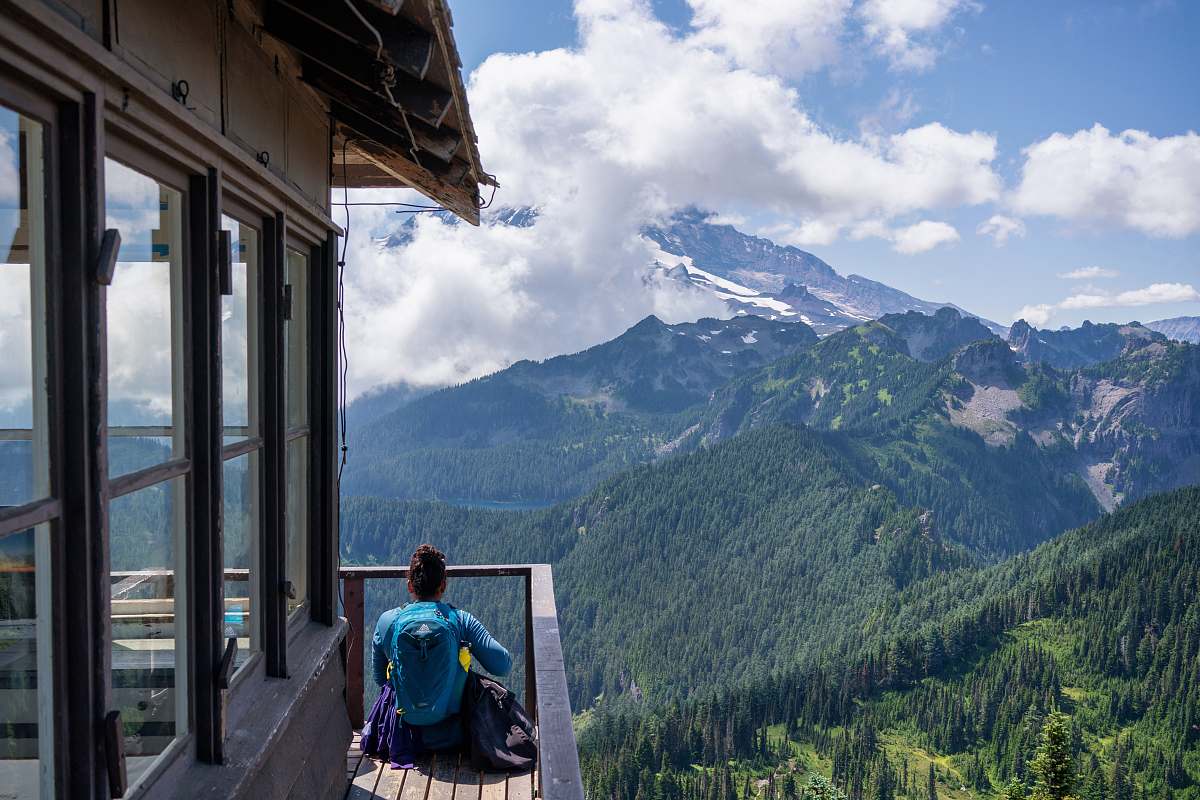 human woman sitting on wooden dock front of mountain at daytime outdoors