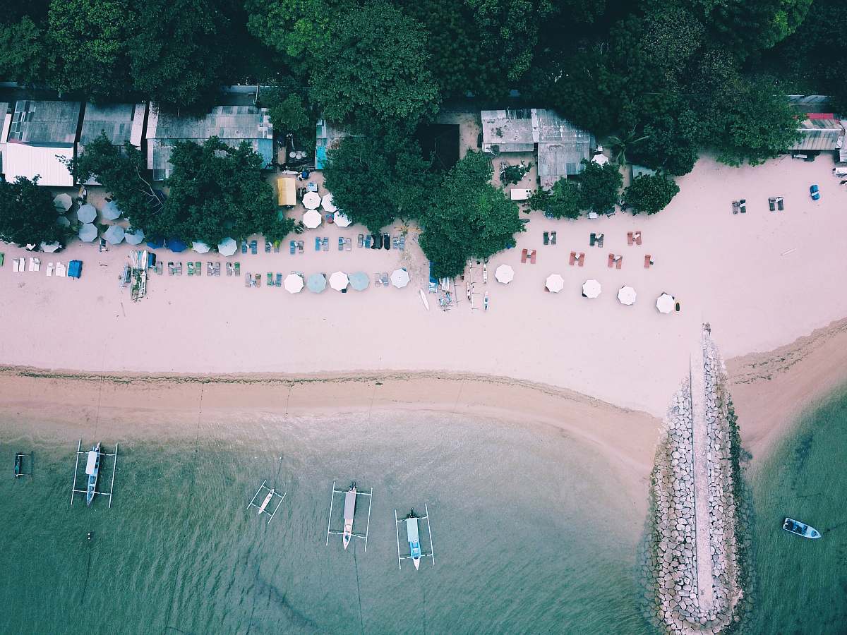 bali beach surrounded by trees and boats on ocean during daytime aerial view