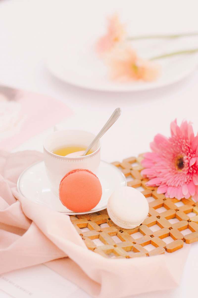 flower two orange and white macaroons beside white ceramic cup with spoon pink