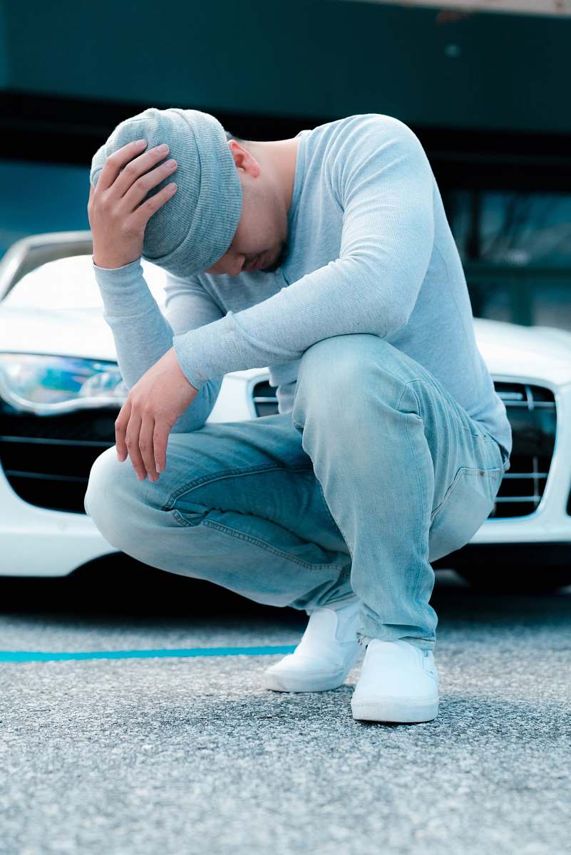 human man wearing grey long-sleeved shirt sitting on ground while holding his knit cap people