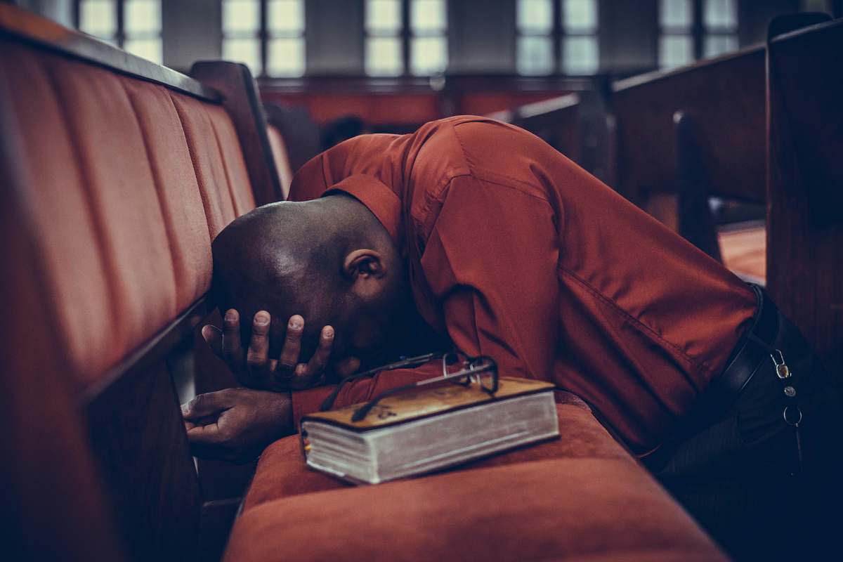 church man in orange top beside eyeglasses on brown book bible