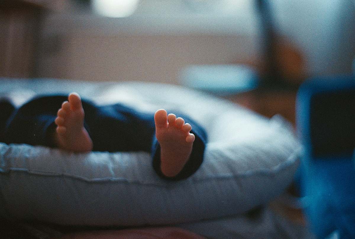 infant closeup photography of baby laying on bed toes