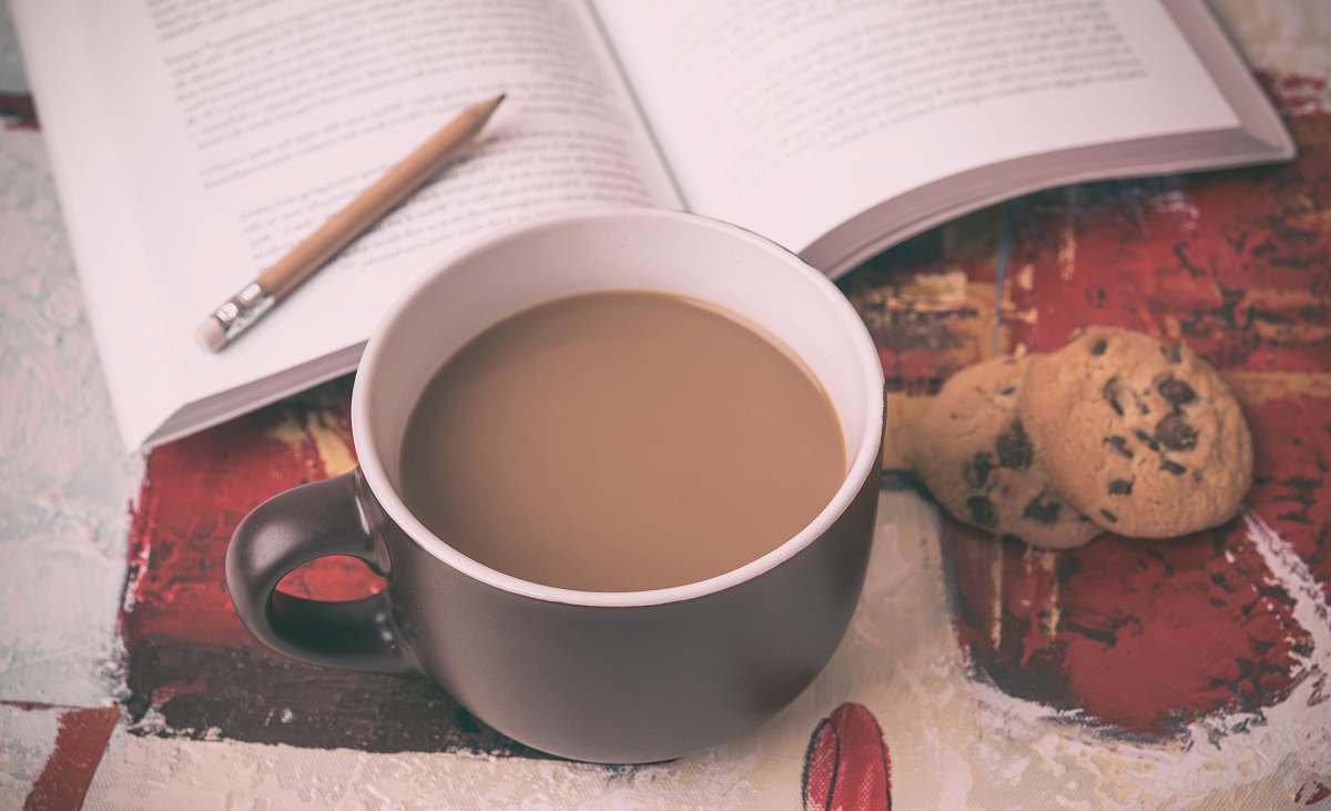 cup beverage filled mug beside cookie and book food